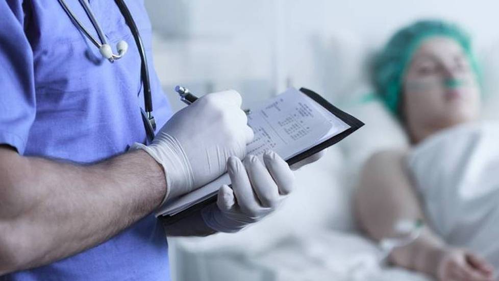 Nurse wearing gloves taking notes near patient in bed