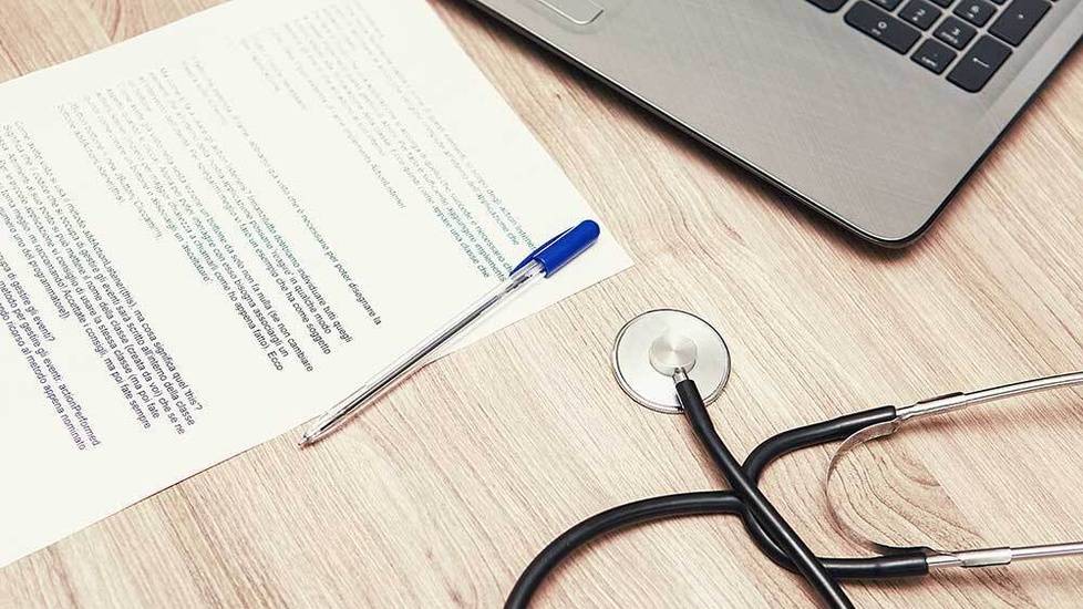 Desk with stethoscope, laptop, and form with pen