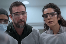 A group of healthcare professionals in protective gowns closely focused in a hospital setting, indicating a critical or intense moment in an emergency room environment.